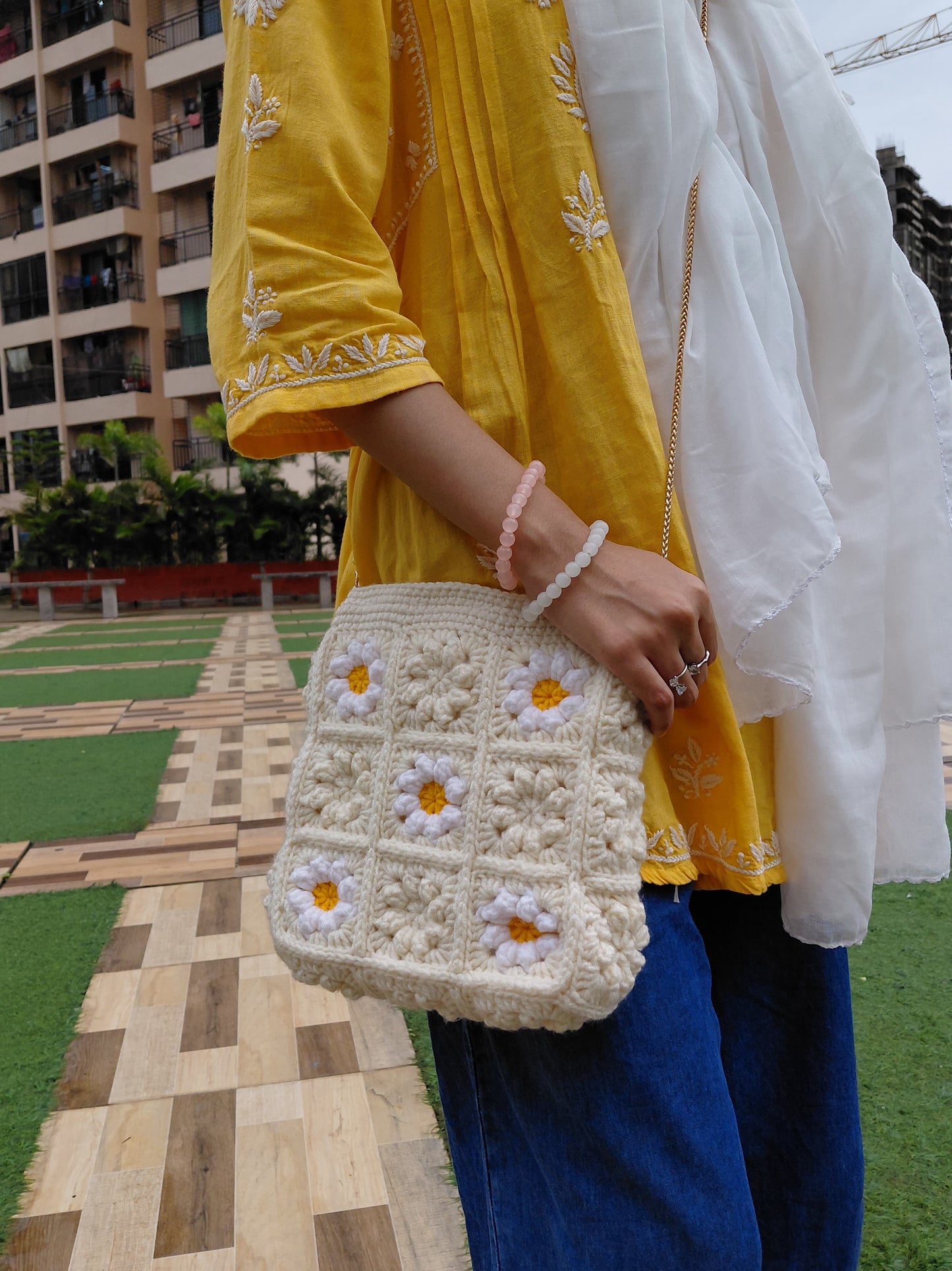 Handcrafted crochet daisy crossbody bag with golden chain, eco-friendly fashion accessory for casual outfits and gifting.