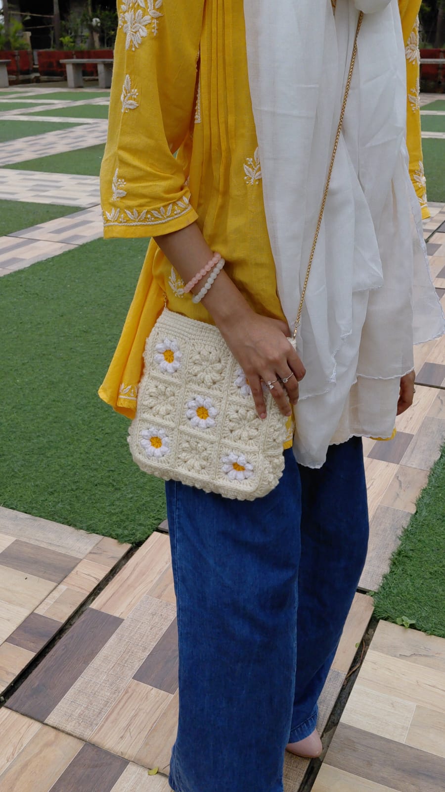 Person wearing a yellow and white outfit with a blue skirt, holding a white handbag with floral patterns on a patterned ground.