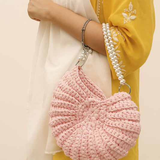 Handmade crochet shell bag in light pink. The unique purse features a conch shell shape and a sophisticated pearl strap. The elegant, beach-style handbag is shown with silver O-rings.